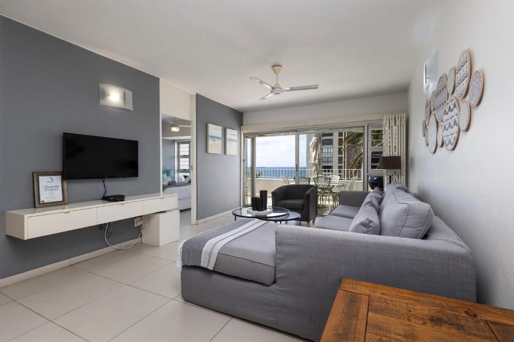 uma sala de estar com um sofá cinzento e uma televisão em 202 Ben Siesta - by Stay in Umhlanga em Durban