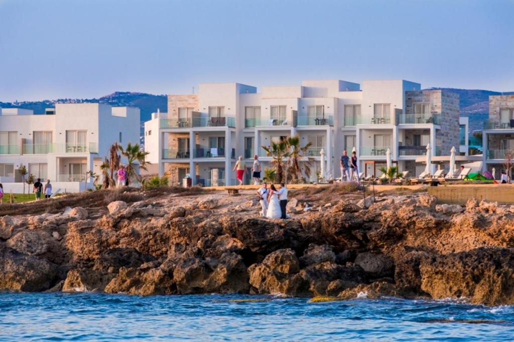 a bride and groom standing on a rocky shoreline near the ocean at Amphora Hotel & Suites in Paphos