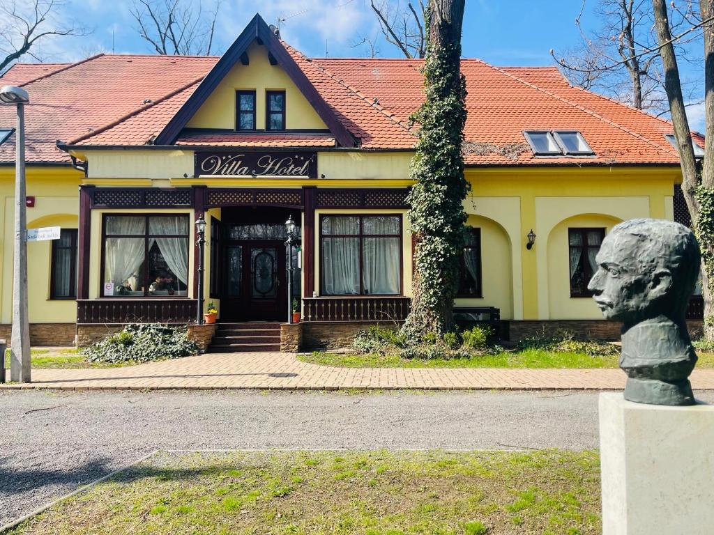 uma casa amarela com uma estátua em frente em Villa Hotel em Debrecen