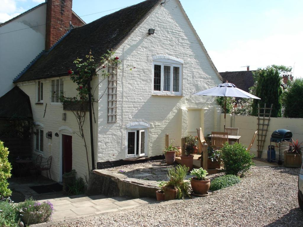 a white house with an umbrella and potted plants at Fosbroke Cottage in Bidford