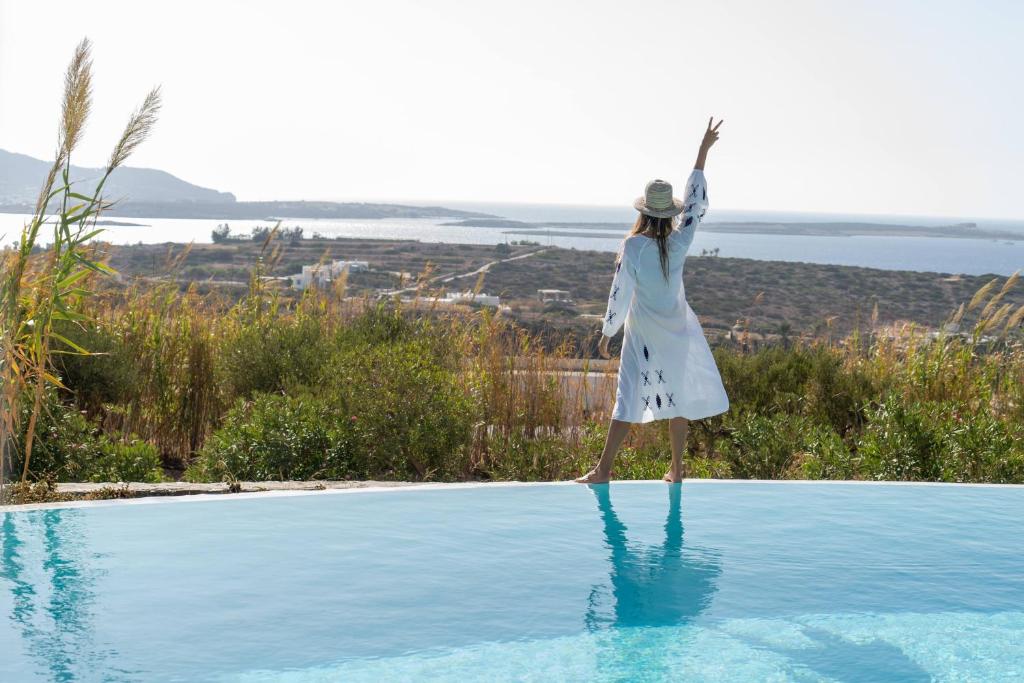 Una donna è in piedi sul bordo di una piscina di Anthemion Paros - Villas & Suites ad Agia Irini Paros