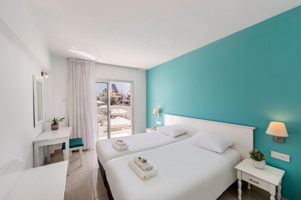 um quarto com 2 camas brancas e uma parede azul em Mia Hotel Apartment em Agia Napa