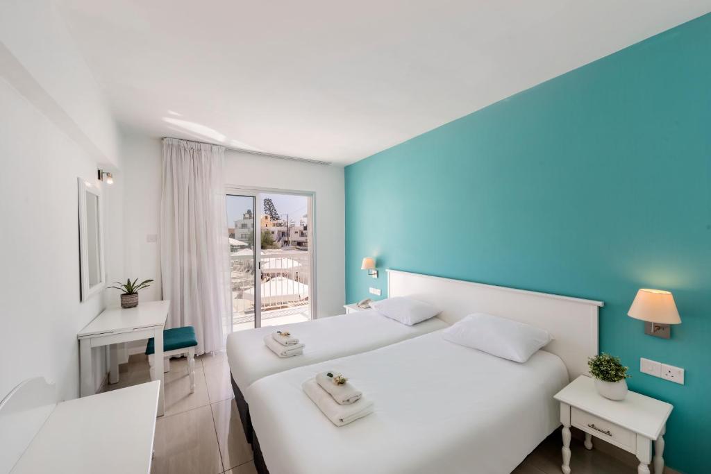 a bedroom with two white beds and a blue wall at Mia Hotel Apartment in Ayia Napa