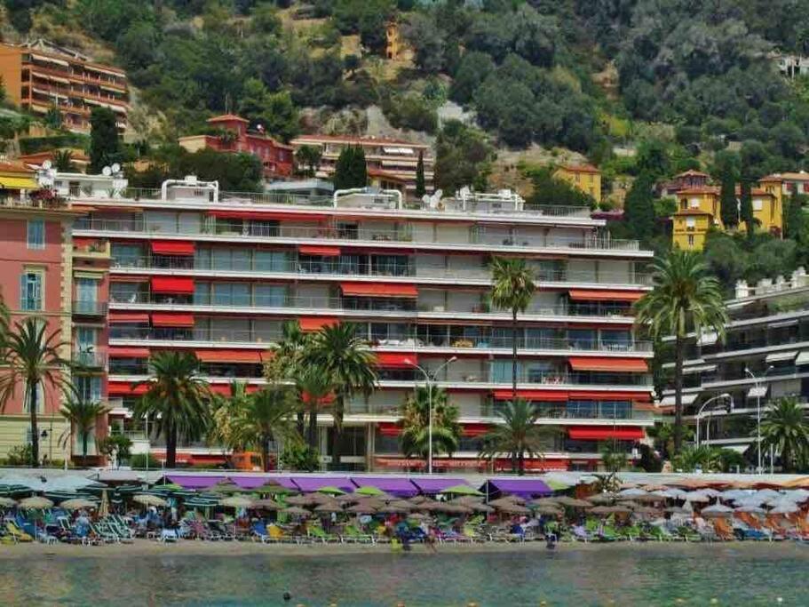 um grande edifício com cadeiras e guarda-sóis na praia em Studio Residence de la Plage, au bord de la mer em Menton