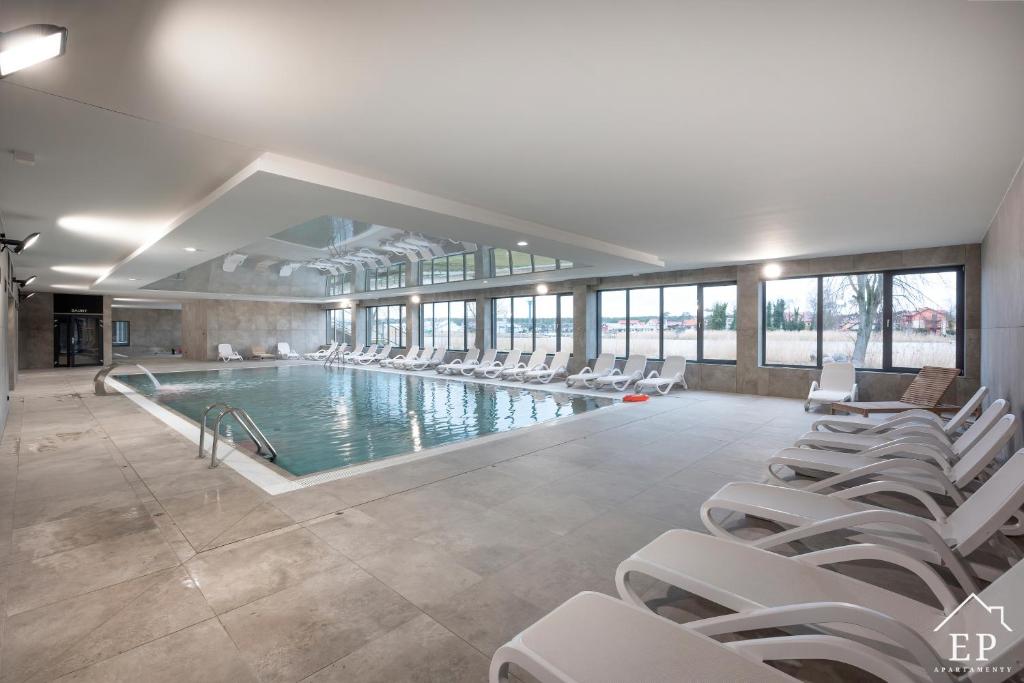 ein großer Pool mit weißen Stühlen in einem Gebäude in der Unterkunft Apartament LAZUROWY Bridge Apartments & Spa z basenem Dziwnów EPapartamenty in Dziwnów