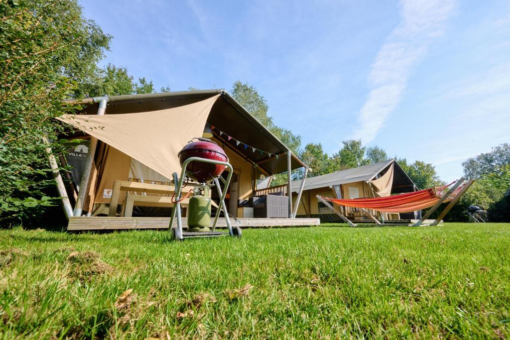 a house with a tent and a hammock in the grass at Glamping Twente in Denekamp