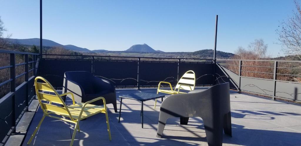 three chairs and a table on a balcony with mountains at La terrasse des volcans in Saint-Genès-Champanelle