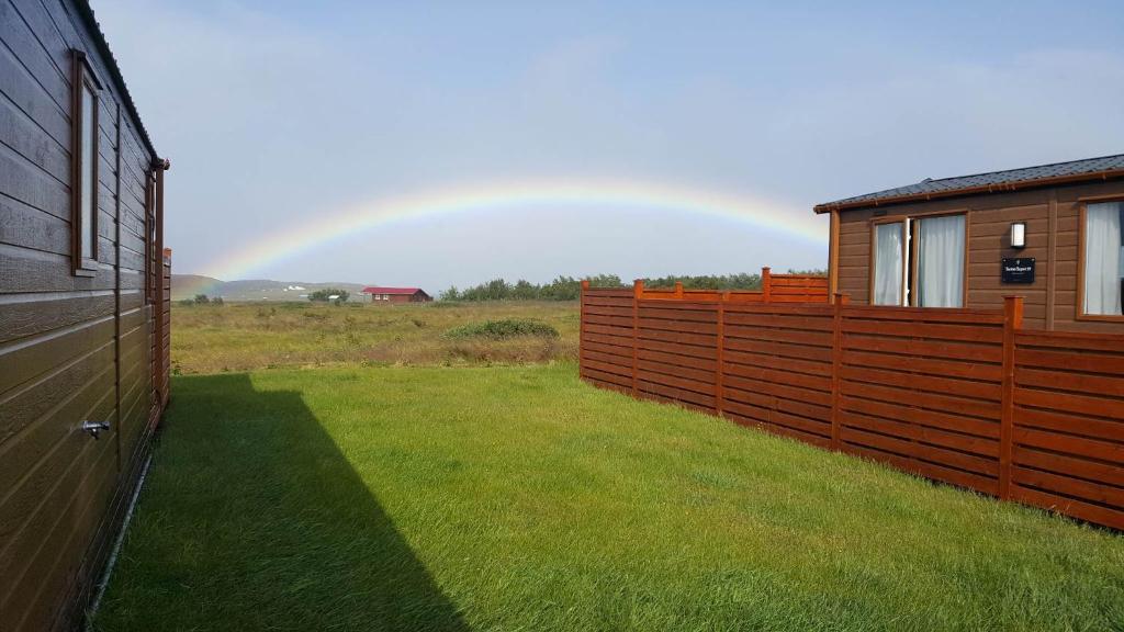a rainbow over a field with a fence and a house at Stuðlaberg in Skagaströnd
