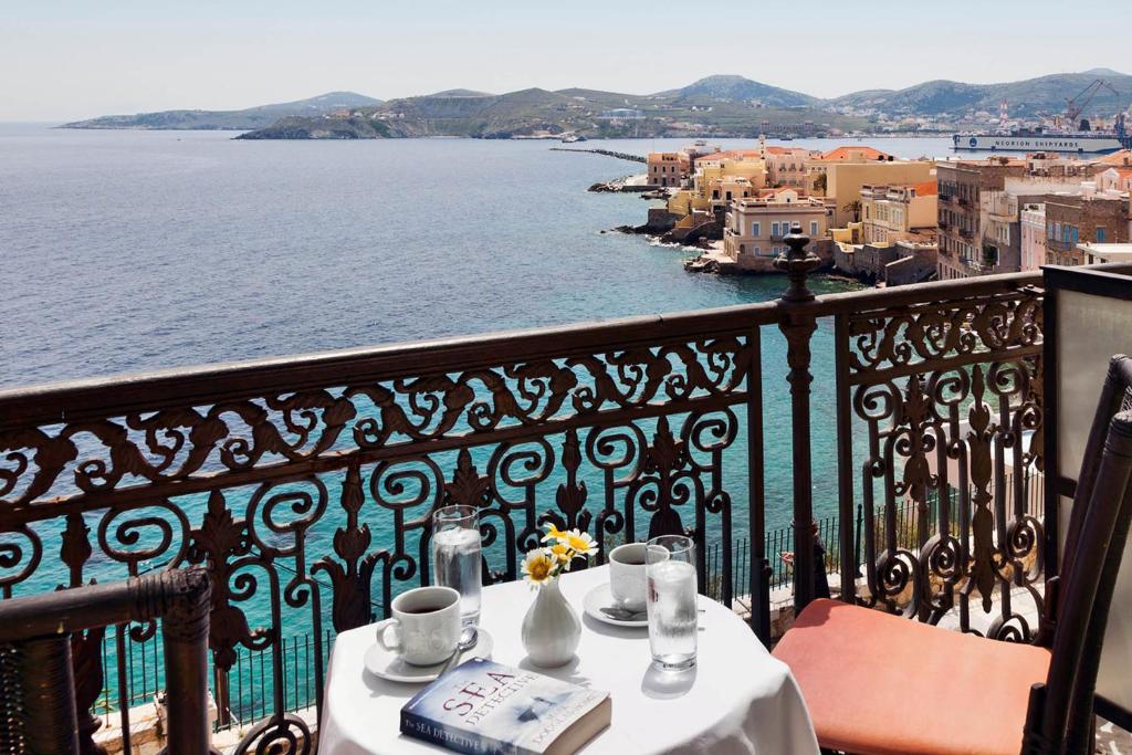 una mesa con bebidas en un balcón con vistas al agua en Syrou Melathron en Ermúpoli