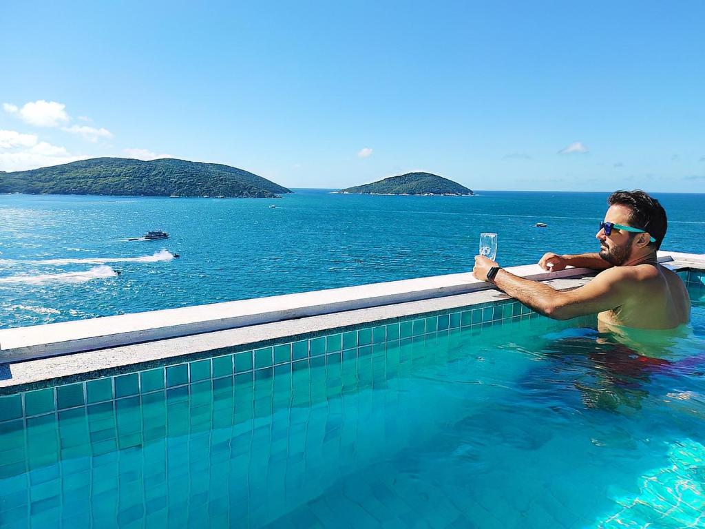 a man sitting in a swimming pool in the water at Marbella Suíte, vista mar, piscina e churrasqueira in Arraial do Cabo