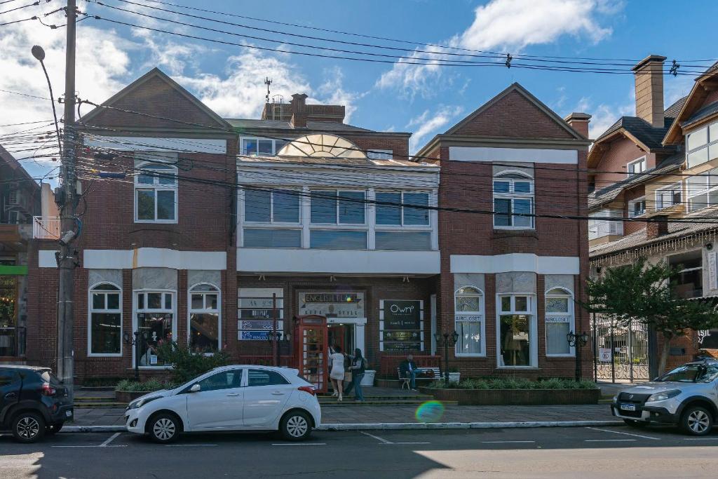 een witte auto geparkeerd voor een bakstenen gebouw bij Rosa Edifício English Place in Gramado