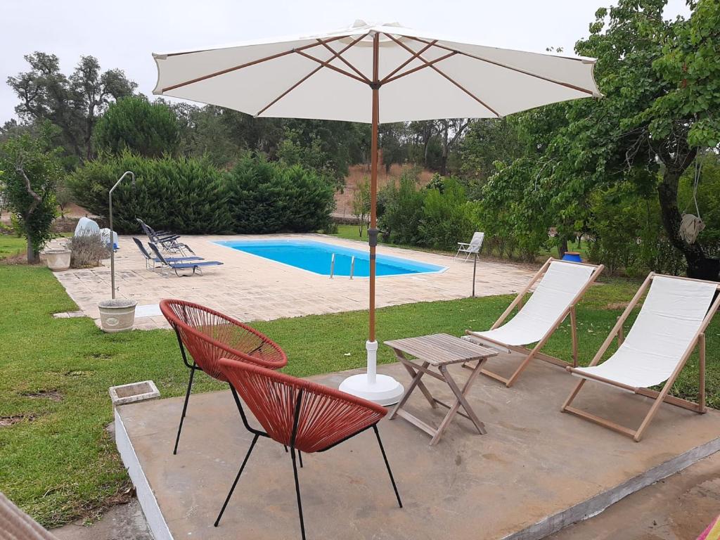 una mesa con sillas y una sombrilla junto a la piscina en Monte das Laranjeiras, en Cortiçadas do Lavre