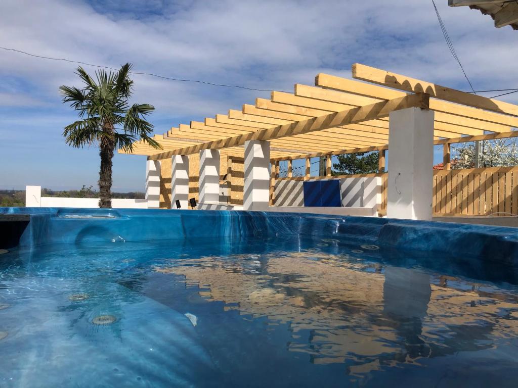 a swimming pool with a wooden pergola and a palm tree at Borbara Apartman in Pázmándfalu