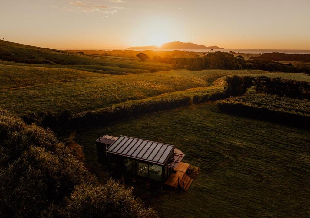 eine Bank auf einem Feld mit Sonnenuntergang im Hintergrund in der Unterkunft Kokomea PurePod in Te Horo