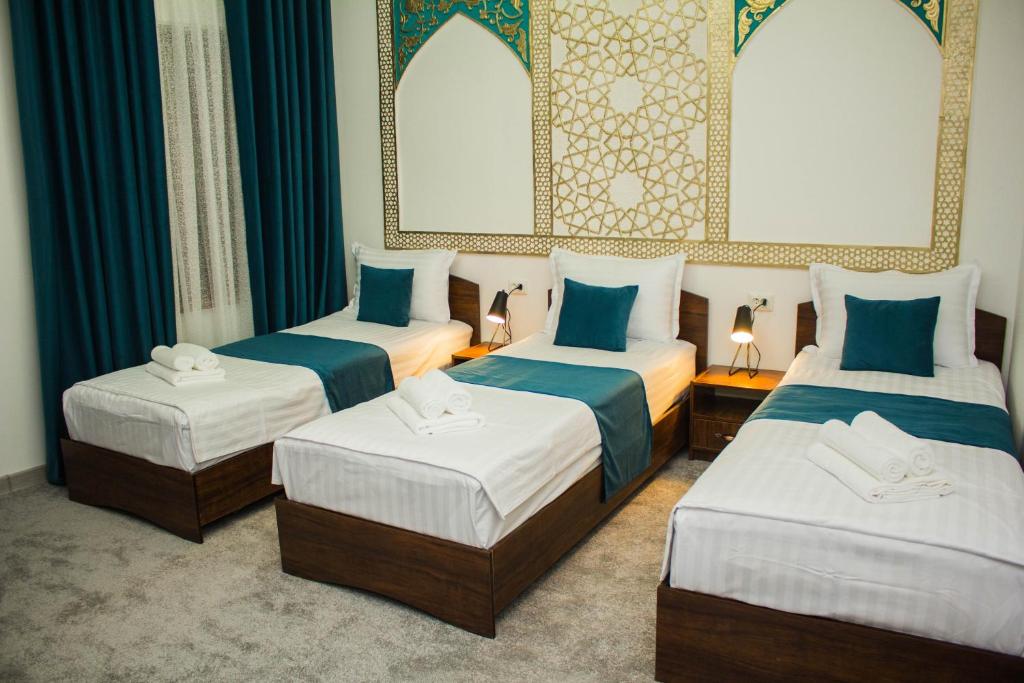 three beds in a room with blue curtains at Jahangir Boutique Bukhara in Bukhara