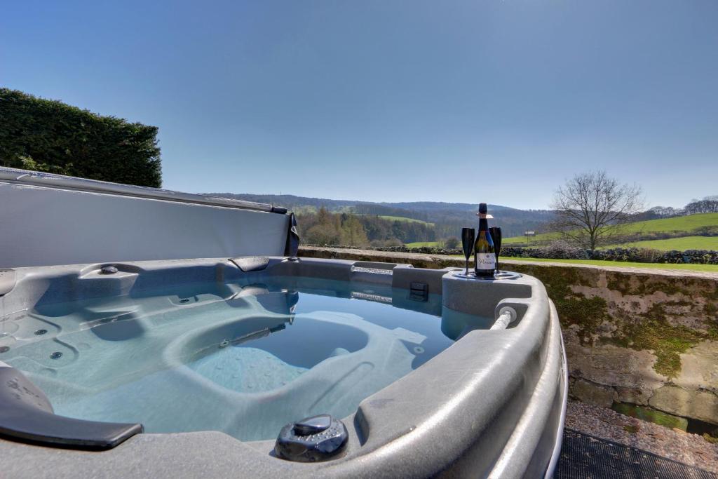 een hot tub op een patio met een fles wijn bij Priesthill HotTub Pool Dog Friendly PeakDistrict in Stanton in Peak