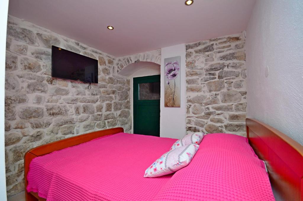 1 dormitorio con 1 cama rosa en una pared de piedra en Villa Capo, en Split
