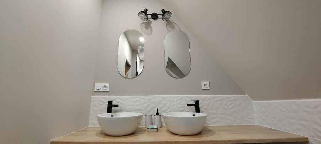 une salle de bain avec deux lavabos blancs et deux miroirs dans l'établissement Les Délices de la Vie, à Le Mesnil-Germain