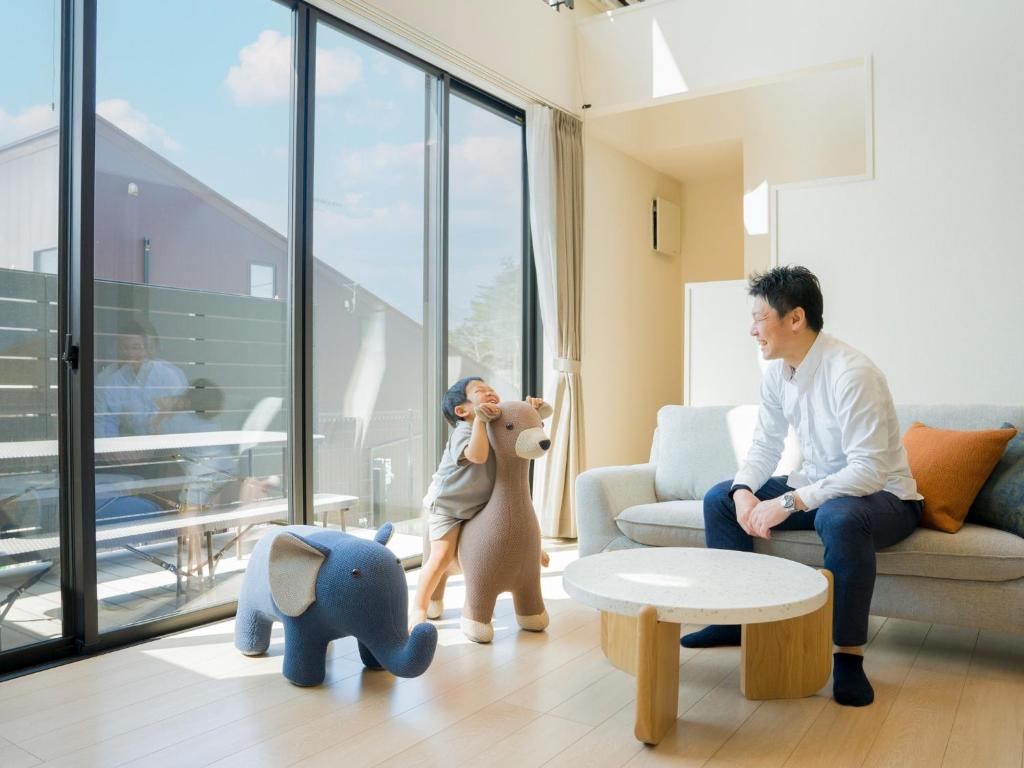 einem Mann, der in einem Wohnzimmer mit einem Kind und Spielzeug sitzt in der Unterkunft Rakuten STAY VILLA Yatsugatake - 106 Family Room - in Hokuto