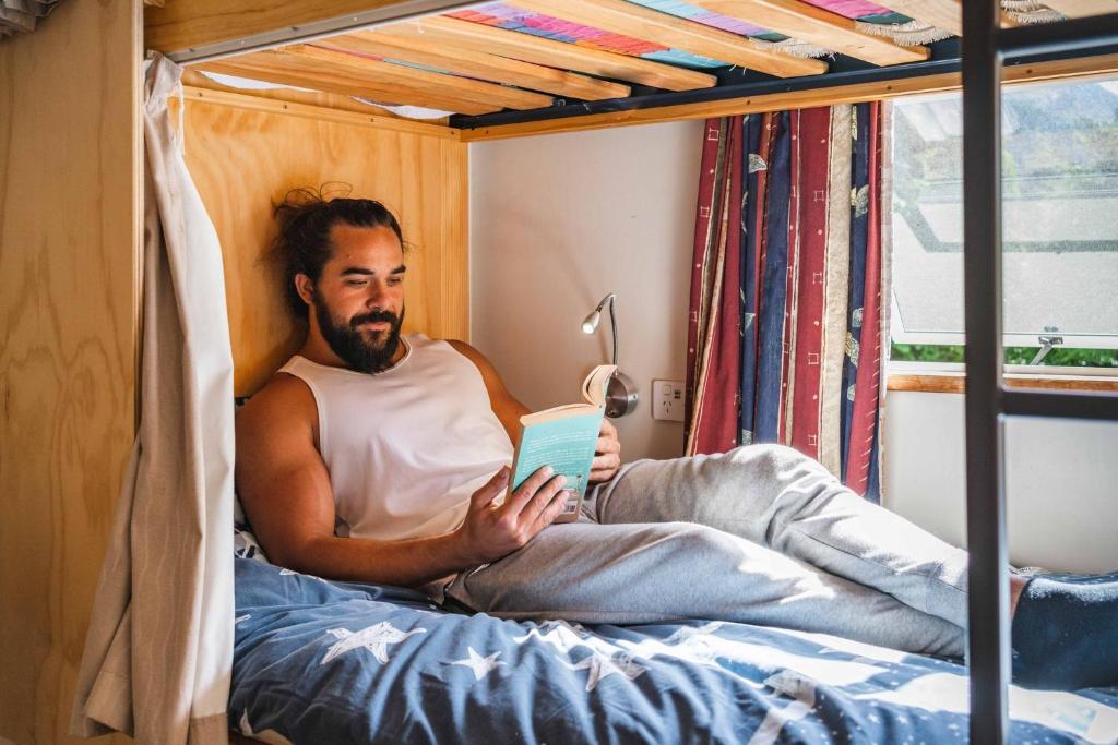 a man sitting on a bed reading a book at The Flaming Kiwi Backpackers in Queenstown