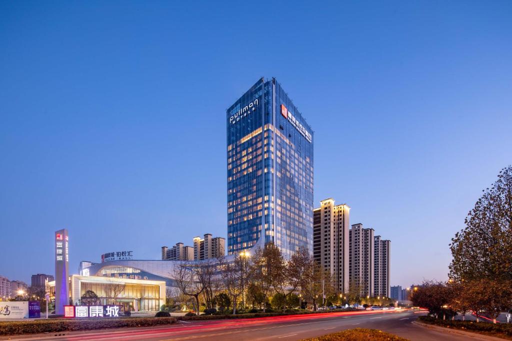 a tall glass building in a city at night at Pullman Huai'an 淮安铂尔曼酒店 in Huai'an
