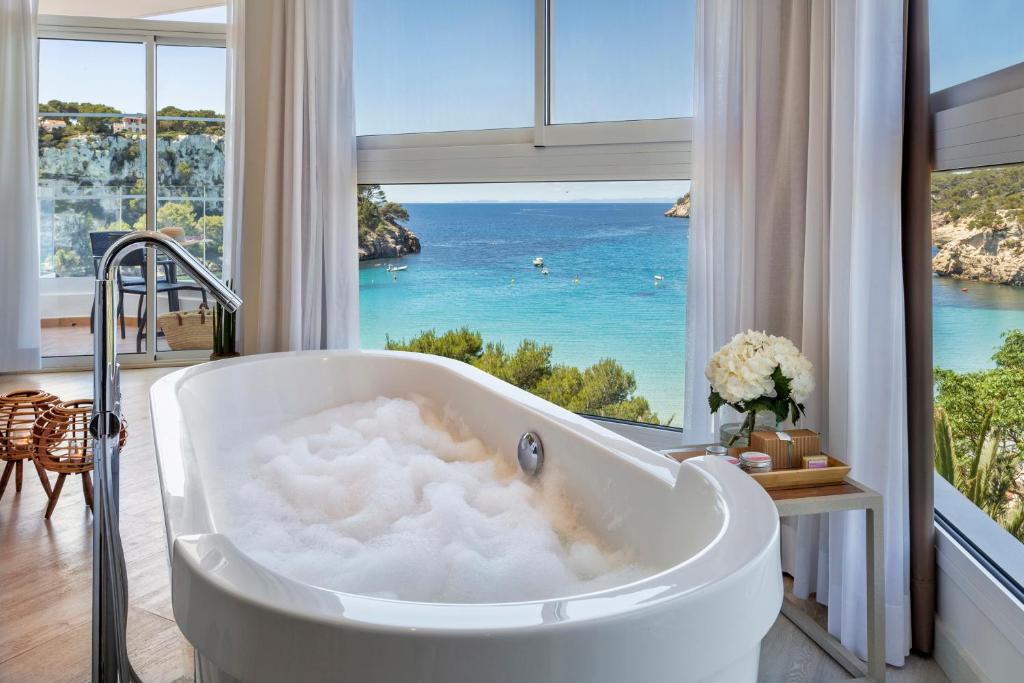 a bath tub in a bathroom with a view of the ocean at Meliá Cala Galdana in Cala Galdana