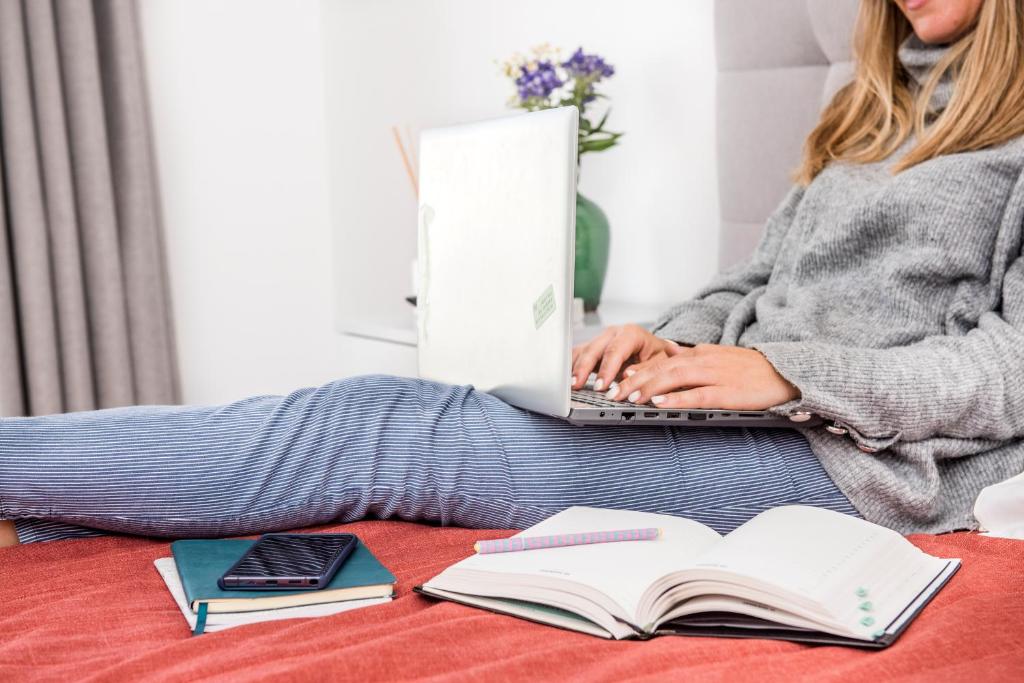 a woman sitting on a bed with a laptop and books at River View Boutique Apts in Ayia Napa