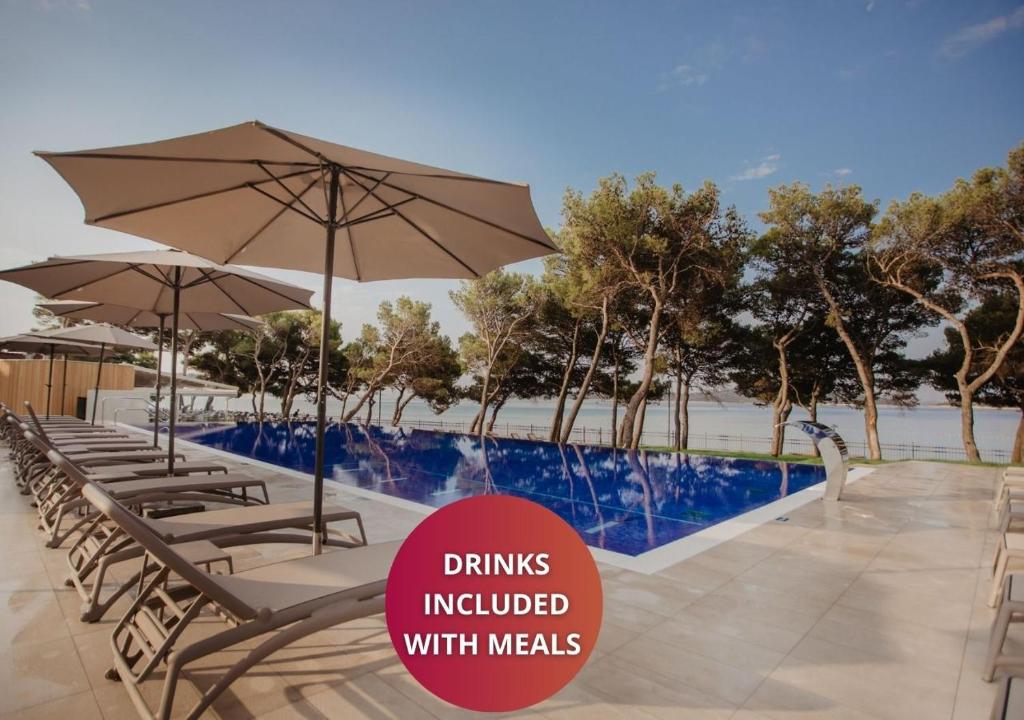 a row of chairs with umbrellas next to a pool at Hotel Punta in Vodice