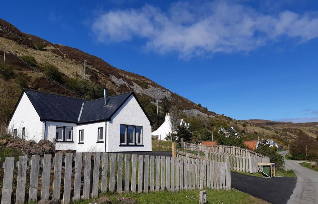 a white house with a fence next to a hill at Bay View Bungalow in Uig