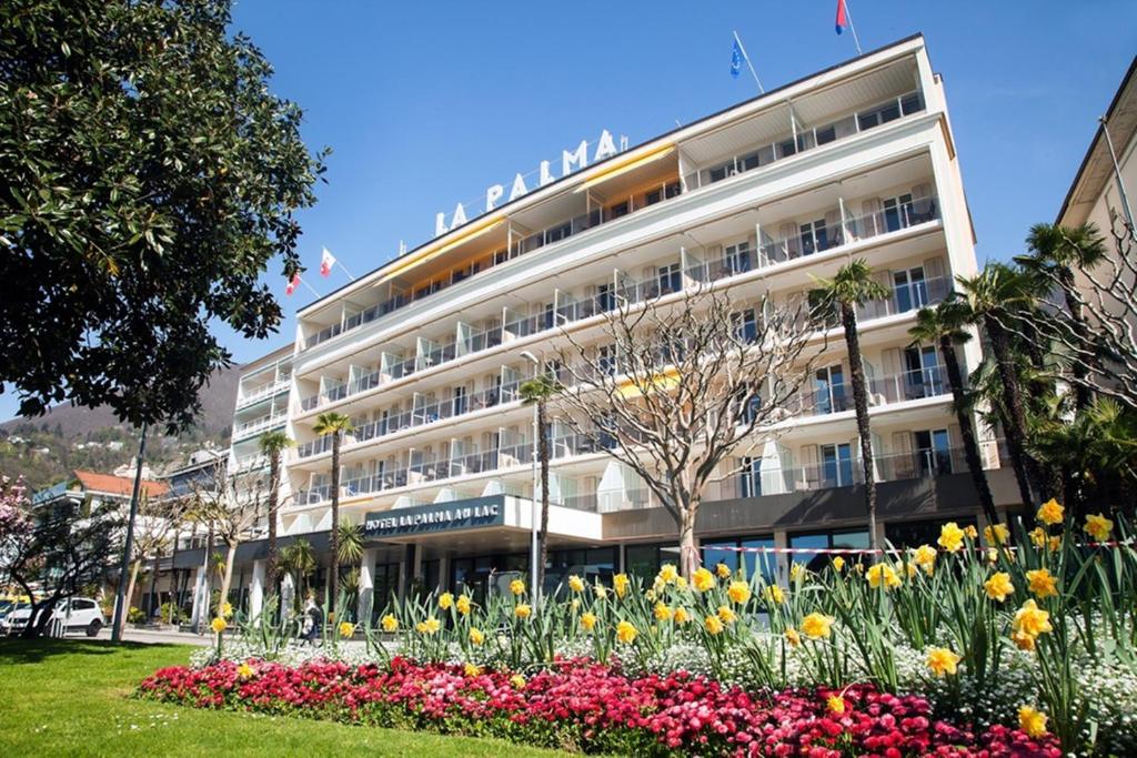 un grand bâtiment avec des fleurs devant lui dans l'établissement Hotel la Palma au Lac, à Locarno