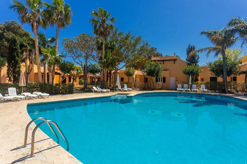 a large swimming pool with palm trees and buildings at S'avarqueta in Son Xoriguer