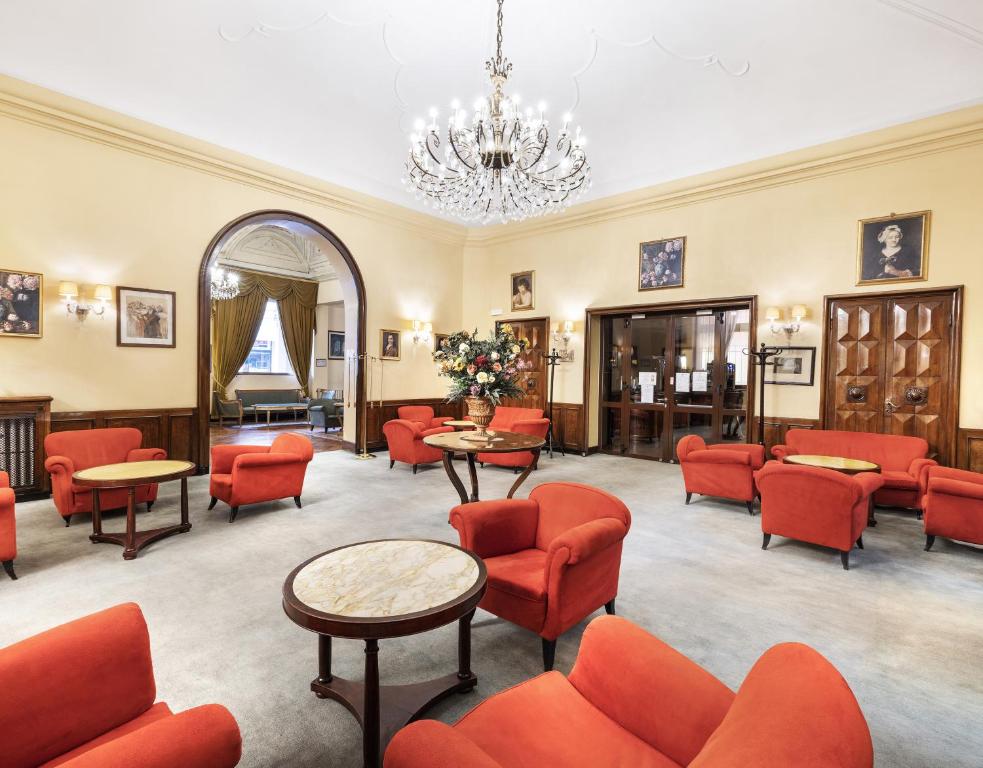 une salle d'attente avec des chaises rouges, des tables et un lustre dans l'établissement Hotel Palace Bologna Centro, à Bologne