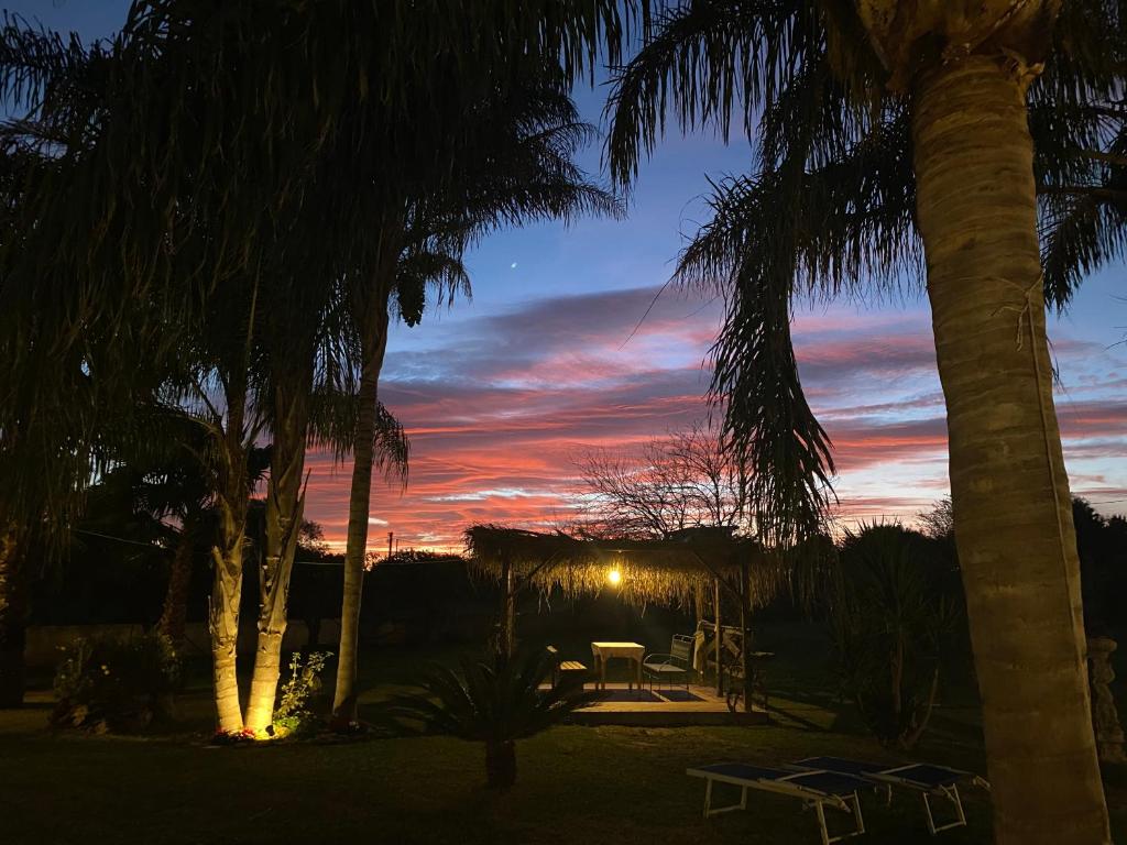 een zonsondergang met een tafel en stoelen onder palmbomen bij Oasi delle palme in Augusta