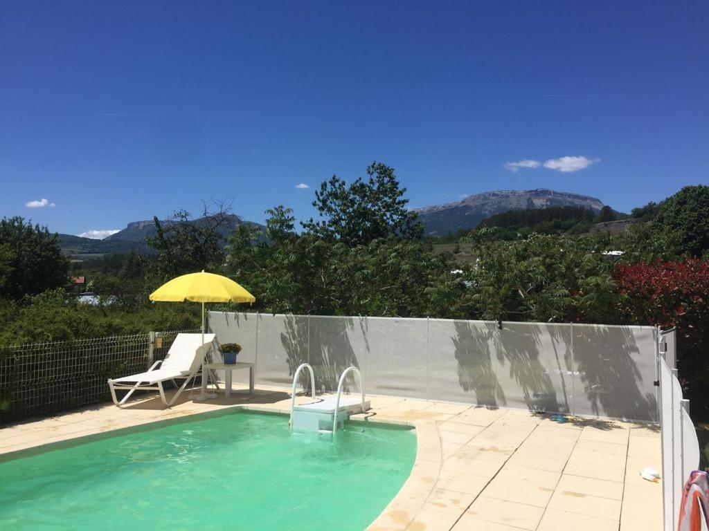 a swimming pool with a yellow umbrella and a chair and a table at Villa les Rosiers in Tallard