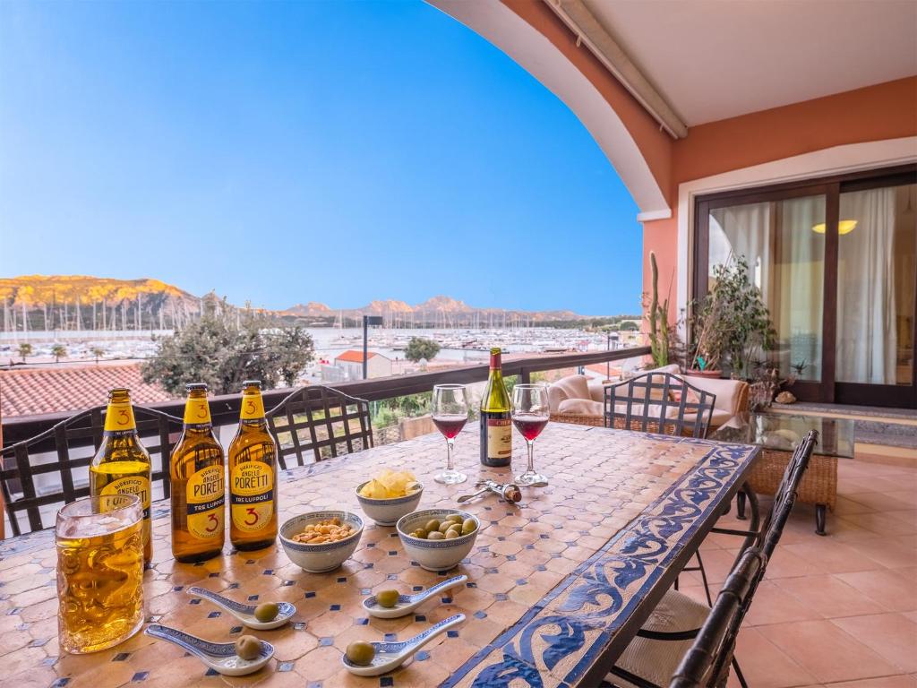 uma mesa com garrafas e copos de vinho numa varanda em Sardinia Family Villas - Cannigione Beach Apartments em Cannigione