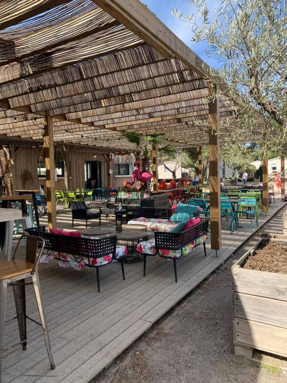 a wooden deck with tables and chairs under a pergola at Mobil home Camping 4* La Falaise Narbonne Plage in Narbonne-Plage