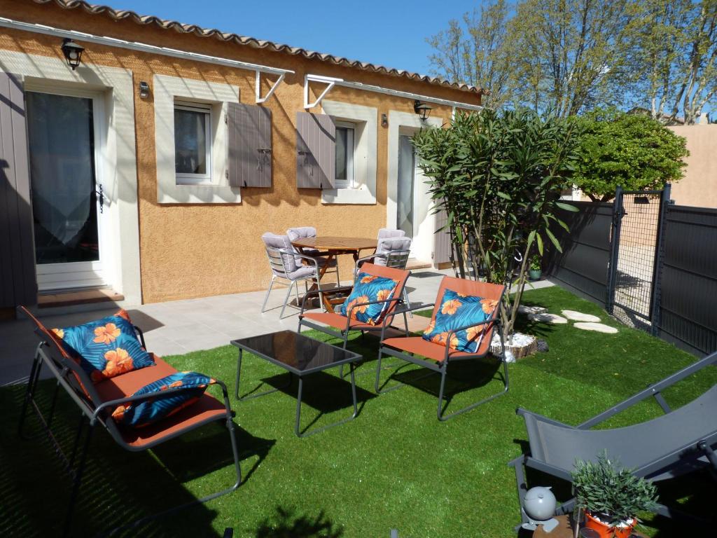 d'une terrasse avec des chaises et une table sur une pelouse. dans l'établissement appart cosy avec son exterieur chaleureux,piscine et parking prive, à Fontvieille