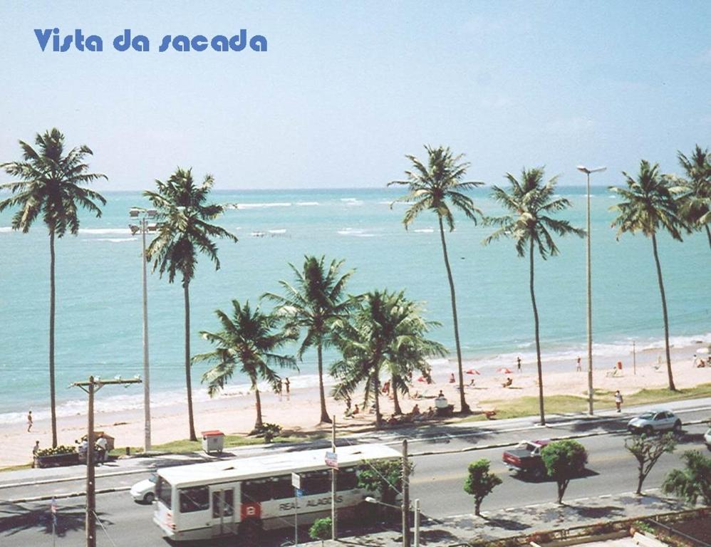 a bus driving down a road near a beach with palm trees at Ap Cote com Vista para Mar e Bicicletas in Maceió