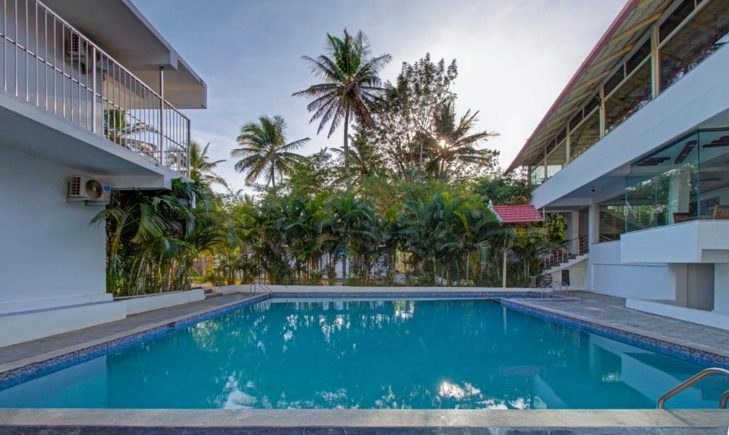 a swimming pool in front of a house with palm trees at Treebo Trend Coorg Dew Drops in Kushālnagar