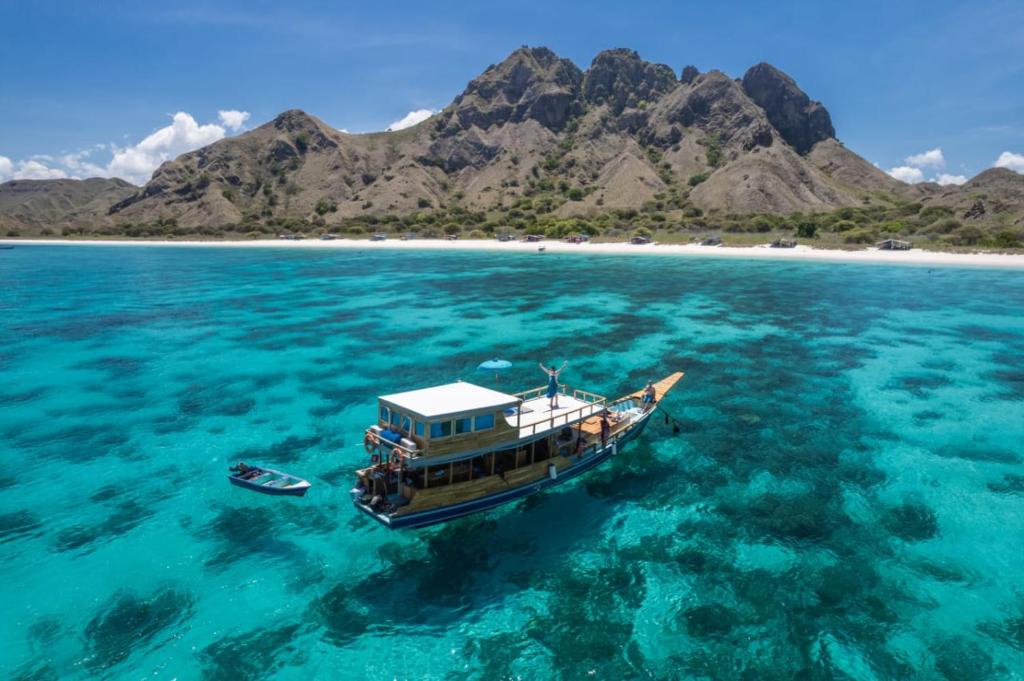 a boat floating in the water near a beach at Komodo Tour 1-6 Pax 2 Days 1Night in Labuan Bajo