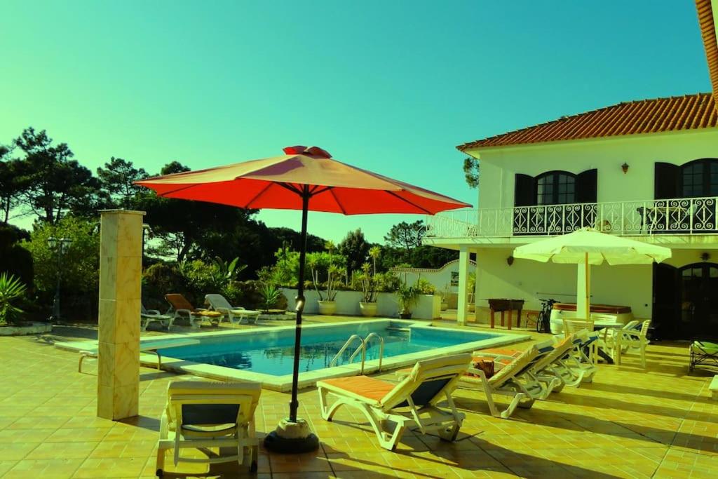 una casa y una piscina con sombrilla y sillas rojas en Casa Piscina Aquecida para 10 adultos Zona Sintra, junto praia, en Colares