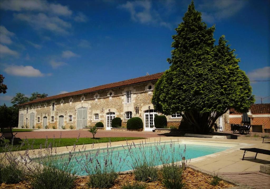 un gran edificio de piedra con un árbol y una piscina en Les Quintanes, en Suaux