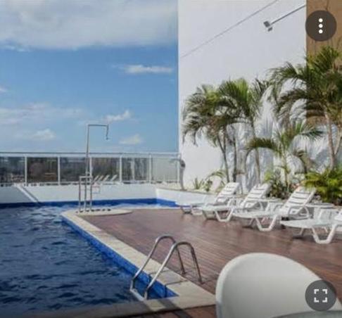 uma piscina com cadeiras brancas e palmeiras num edifício em #SENSACIONAL# PREMIUM HOTEL Manaus AM em Manaus