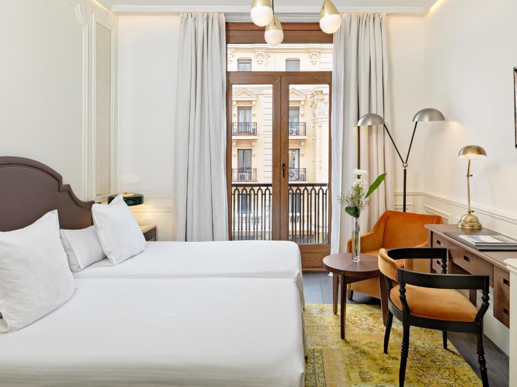 マドリードにあるブティック ホテル H10 ヴィラ デ ラ レイナのベッドとデスクが備わるホテルルームです。