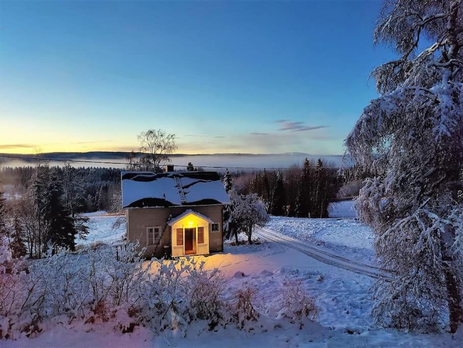 een klein huis met een geel licht in de sneeuw bij Mysigt hus med utsikt över fjäll och älv. in Järpen