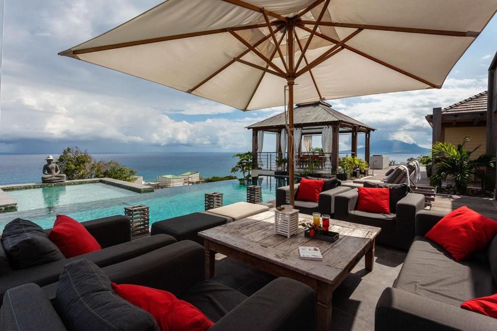 une terrasse avec des canapés, une table et un parasol dans l'établissement Villa L'Oasis, à Oranjestad