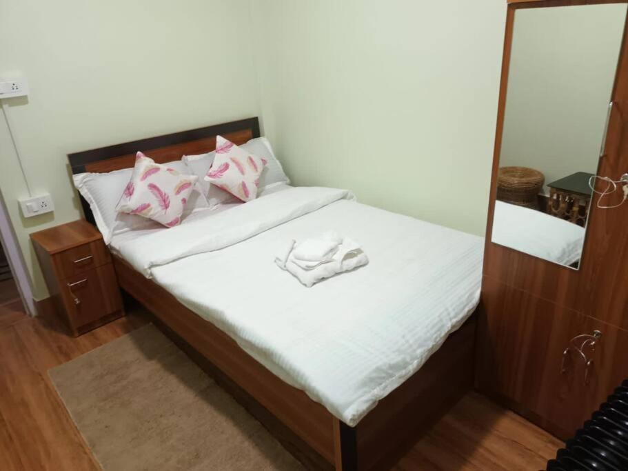 - un lit avec des draps blancs, des oreillers roses et un miroir dans l'établissement Primrose Homestay (A cozy 2 bedroom apartment), à Darjeeling
