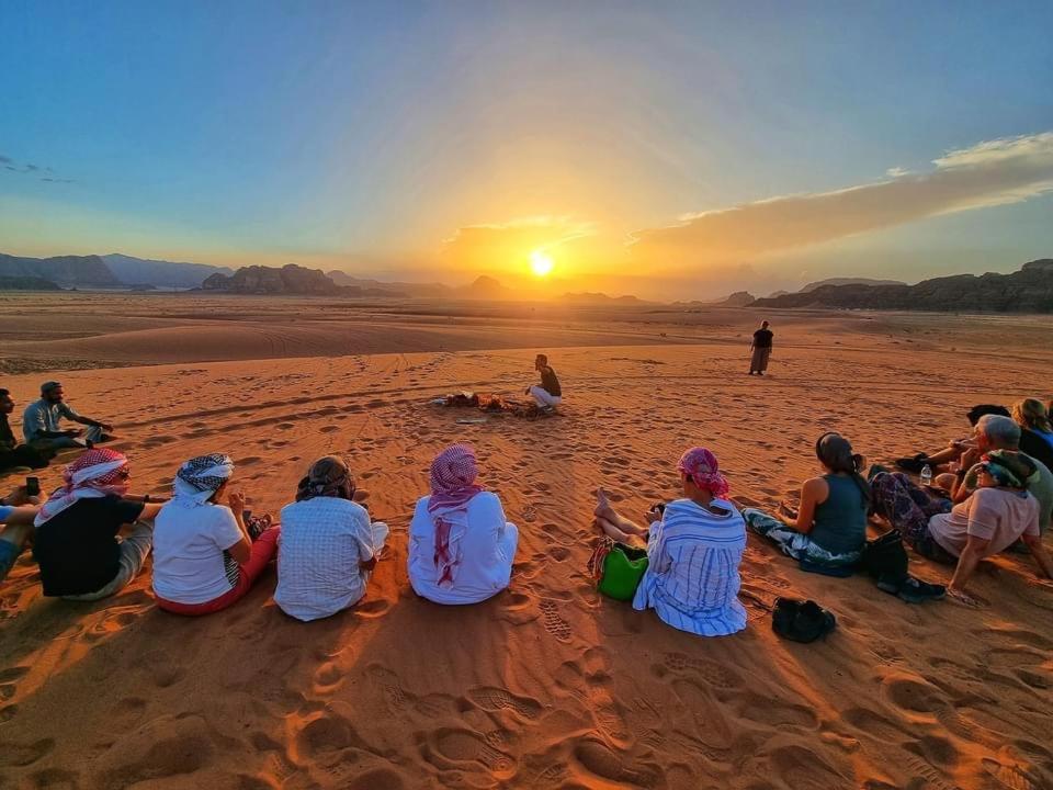a group of people sitting on the beach watching the sunset at Wadi Rum Red Sand Camp in Wadi Rum
