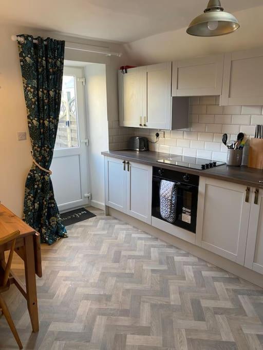 a kitchen with white cabinets and a wooden floor at Centrally located flat with parking in Tetbury