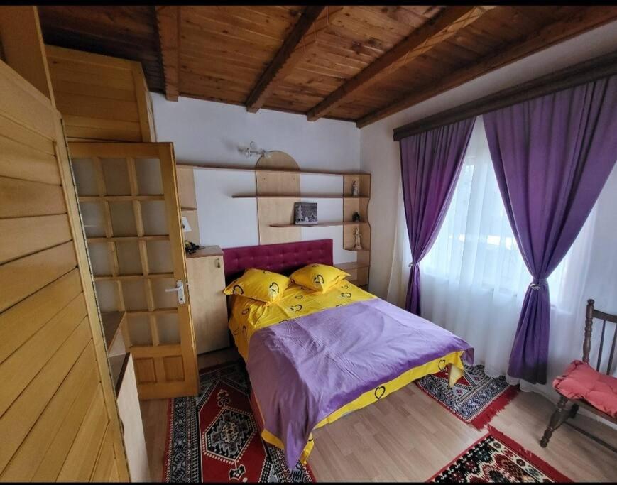 a bedroom with a bed and a window with purple curtains at Casa Roza in Breaza de Sus